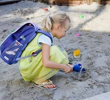 en pige med skoletaske på ryggen leger i en sandkasse
