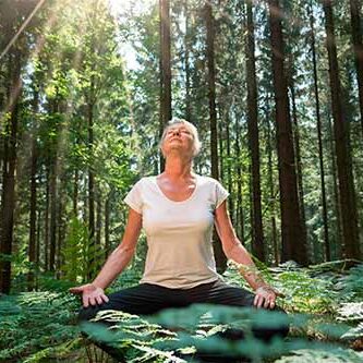 kvinde sidder og mediterer ude i en skov