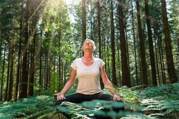 kvinde sidder og mediterer ude i en skov