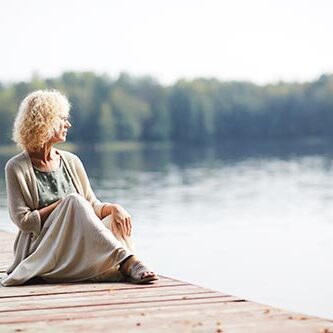 kvinde sidder på bådebro og stirrer ud over sø
