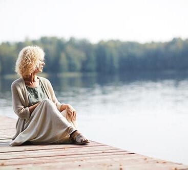 kvinde sidder på bådebro og stirrer ud over sø
