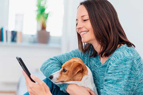glad kvinde holder om sin hund og tjekker sin mobil
