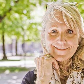 en moden kvinde står udenfor under træer og ser tilfreds ud